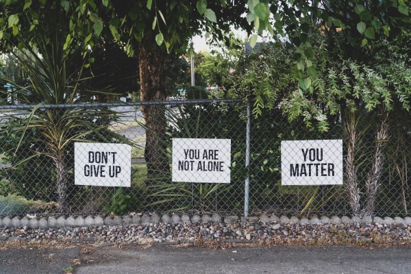 Substance use disorder - image of encouragement signs on a chainlinked fence with some palm trees behind